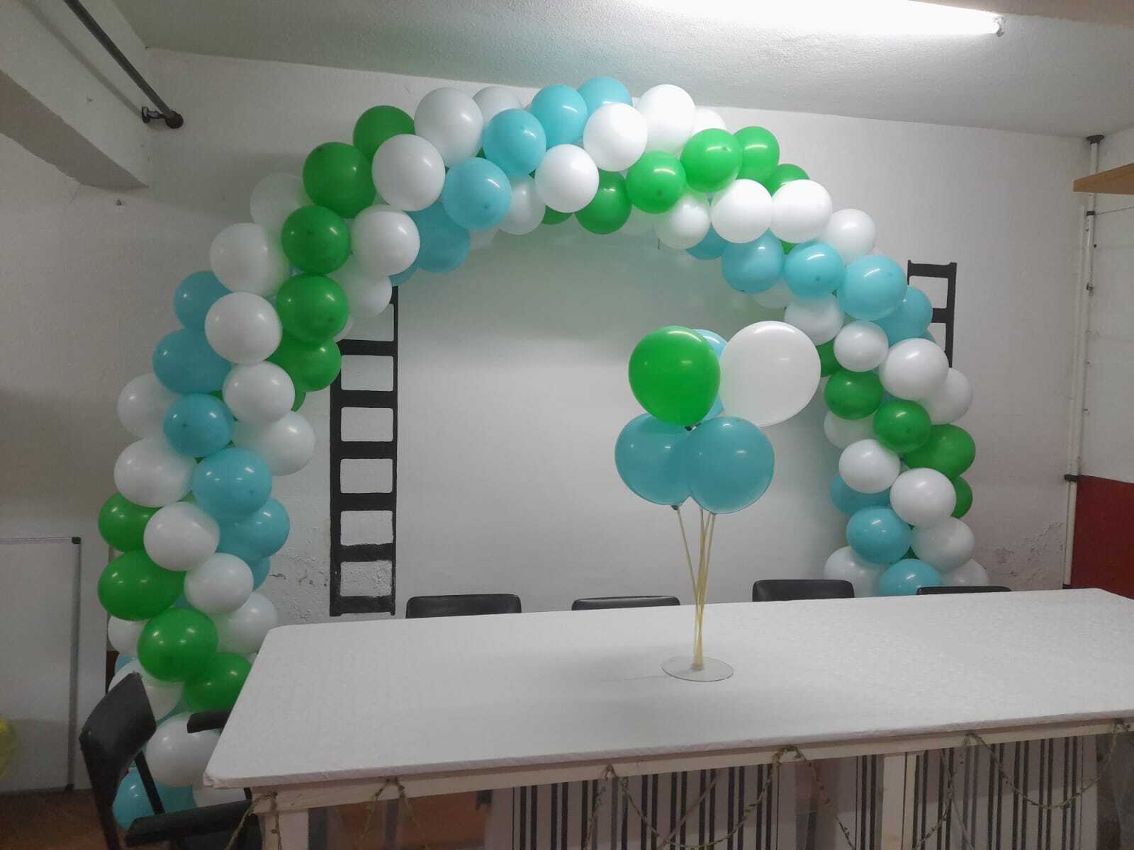 Arco de balões verde, azul e branco a decorar mesa de evento com centro de mesa a condizer